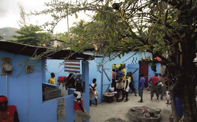 A group of people stand outside a blue building in Carrefour, Haiti.
